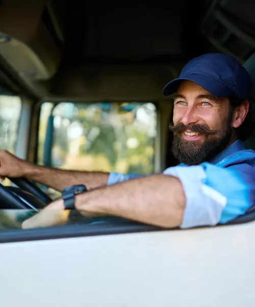 A happy truck driver smiling and looking out his truck's window, providing freight and shipping services across the Midwest