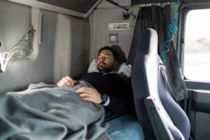 Expert Tips for Lower Back Pain Relief on the Road 3 Tired truck driver sleeping in cabin bed on truck stop. Prioritizing sleep is a good tip for Lower Back Pain Relief on the Road